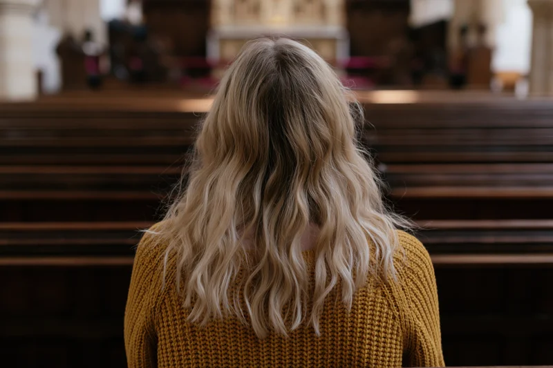 Woman with long blonde hair sitting alone in a church facing the altar