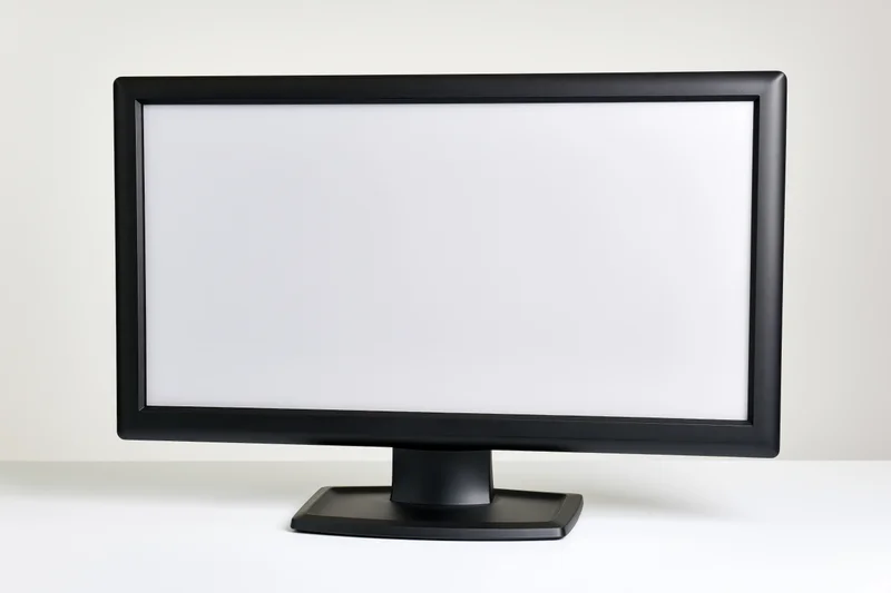 Black widescreen desktop computer monitor with blank white screen on white surface