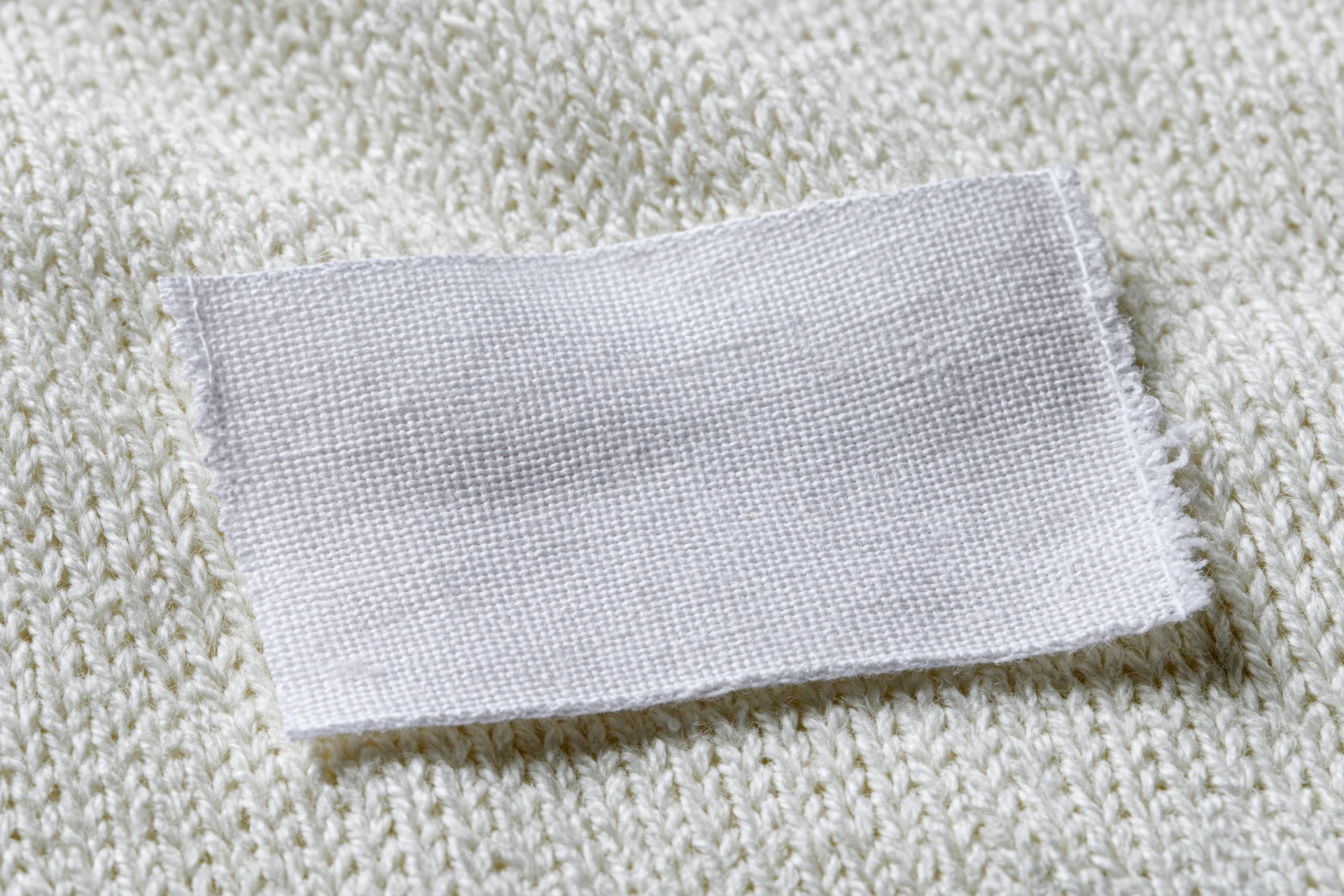 Blank white woven label sewn onto white knitted sweater fabric