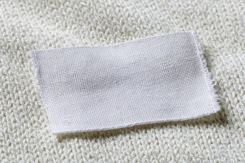 Blank white woven label sewn onto white knitted sweater fabric