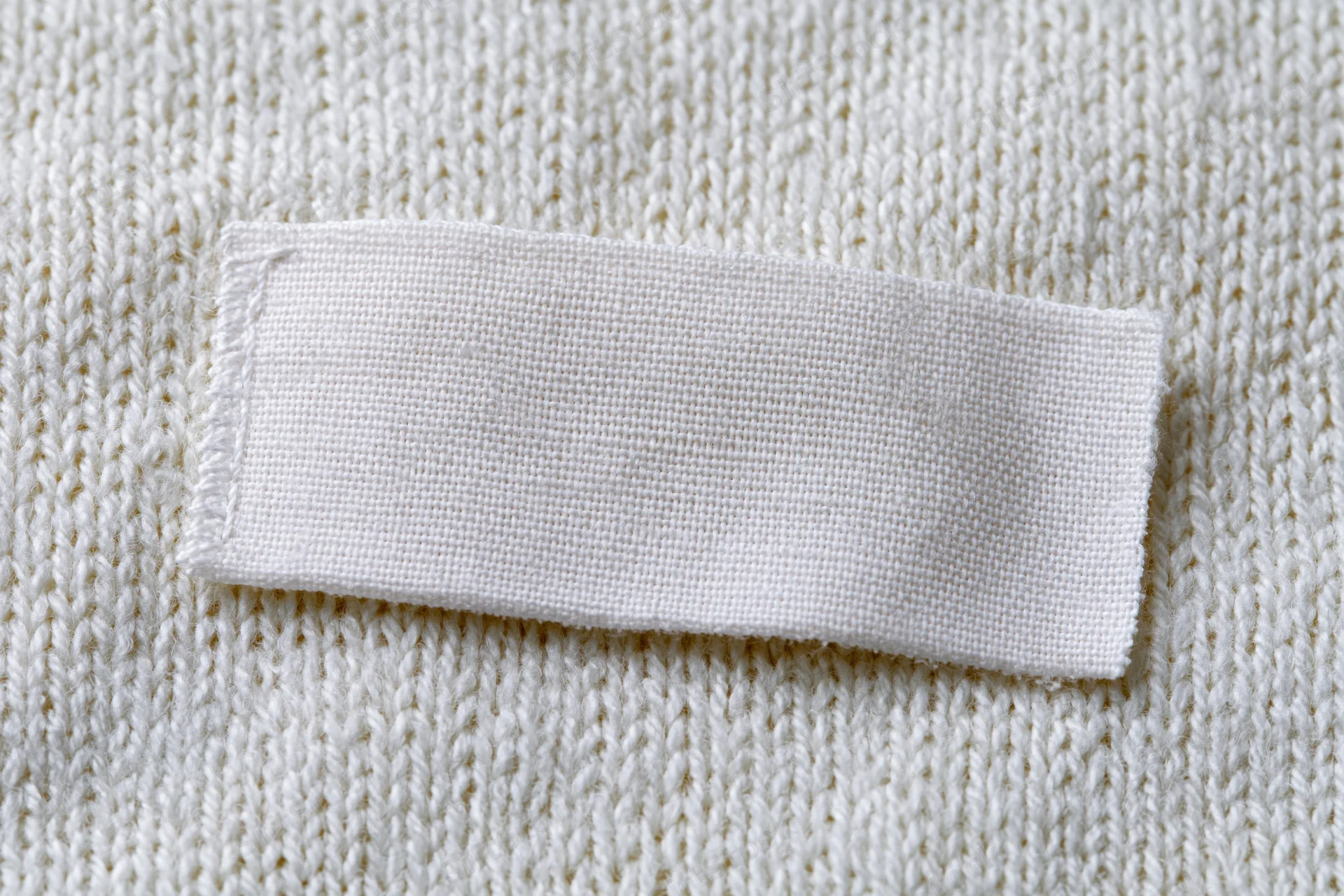 Blank white woven label sewn onto white knitted sweater fabric