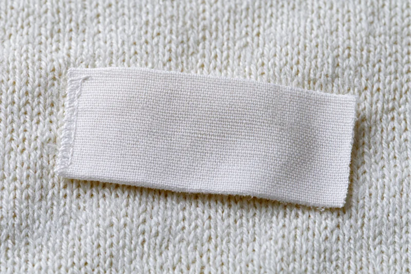 Blank white woven label sewn onto white knitted sweater fabric