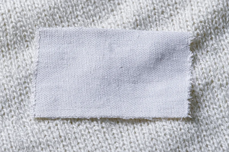 Blank white woven label sewn onto white knitted sweater fabric