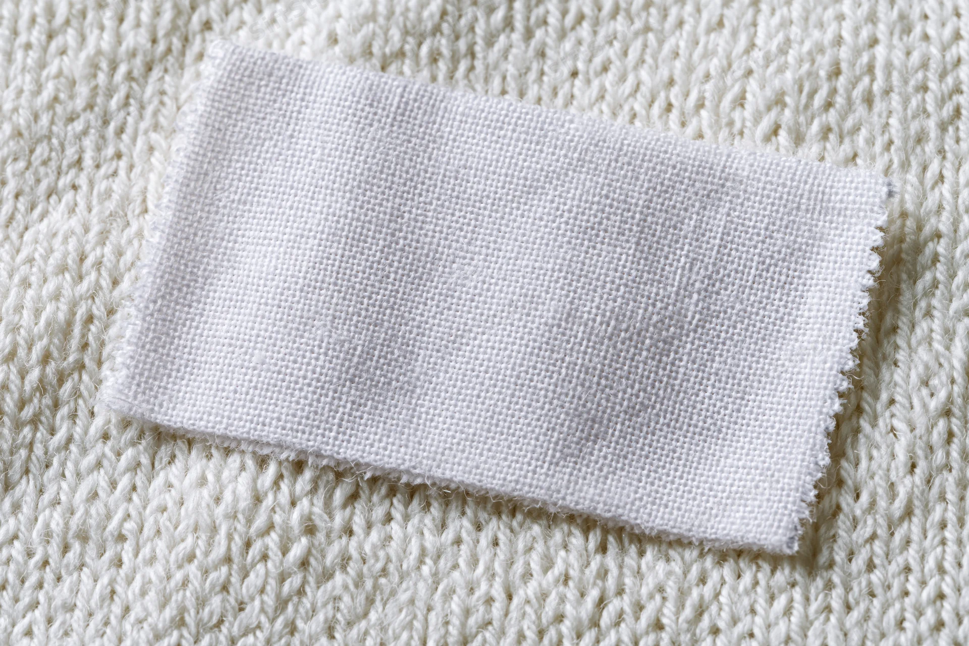 Blank white woven label sewn onto white knitted sweater fabric