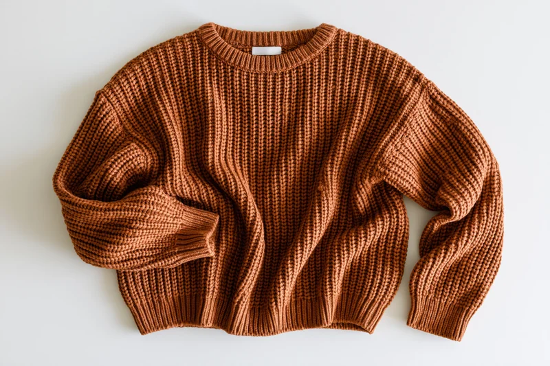 Brown chunky knit sweater laid flat on white surface