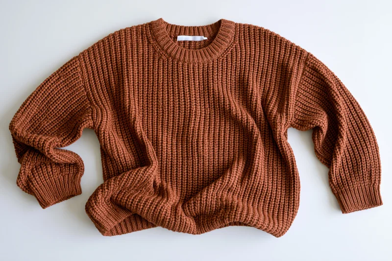 Brown chunky knit sweater laid flat on white surface