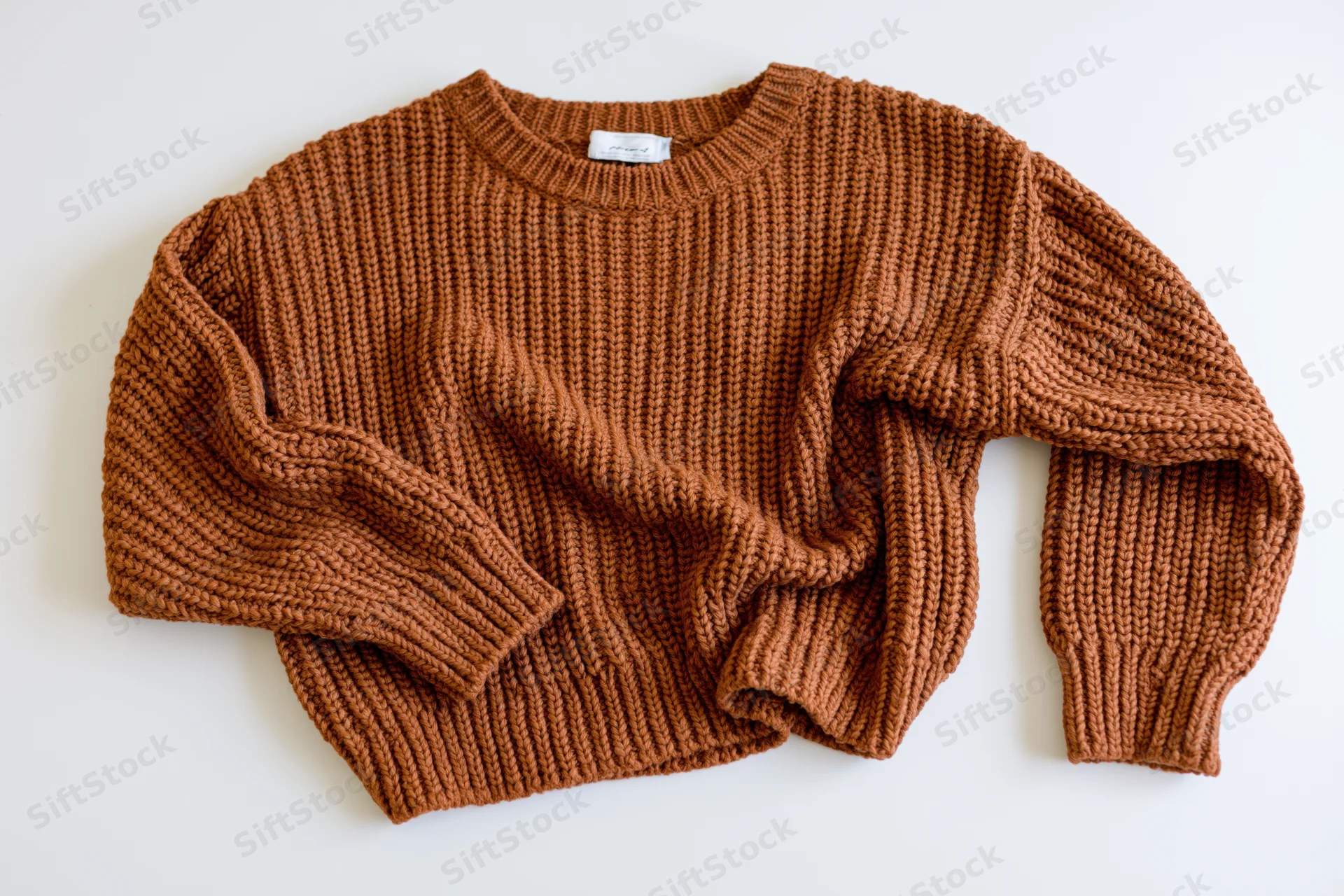 Brown chunky knit sweater folded casually on white surface