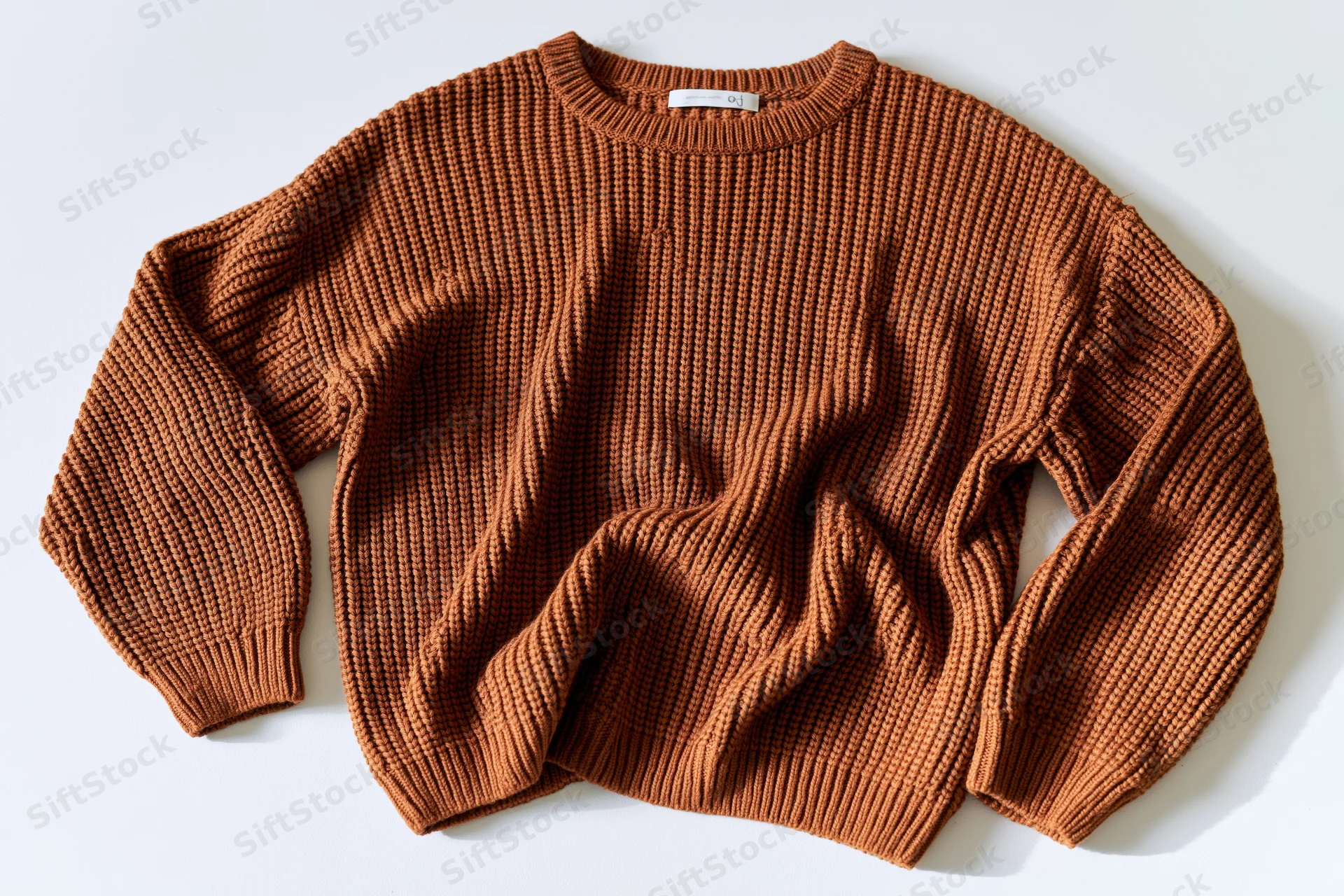 Caramel-brown ribbed knit sweater laid flat on white background