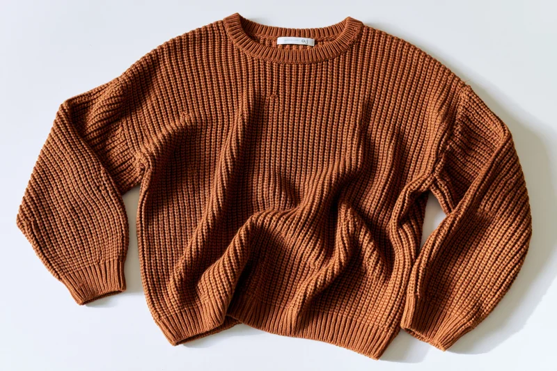 Caramel-brown ribbed knit sweater laid flat on white background