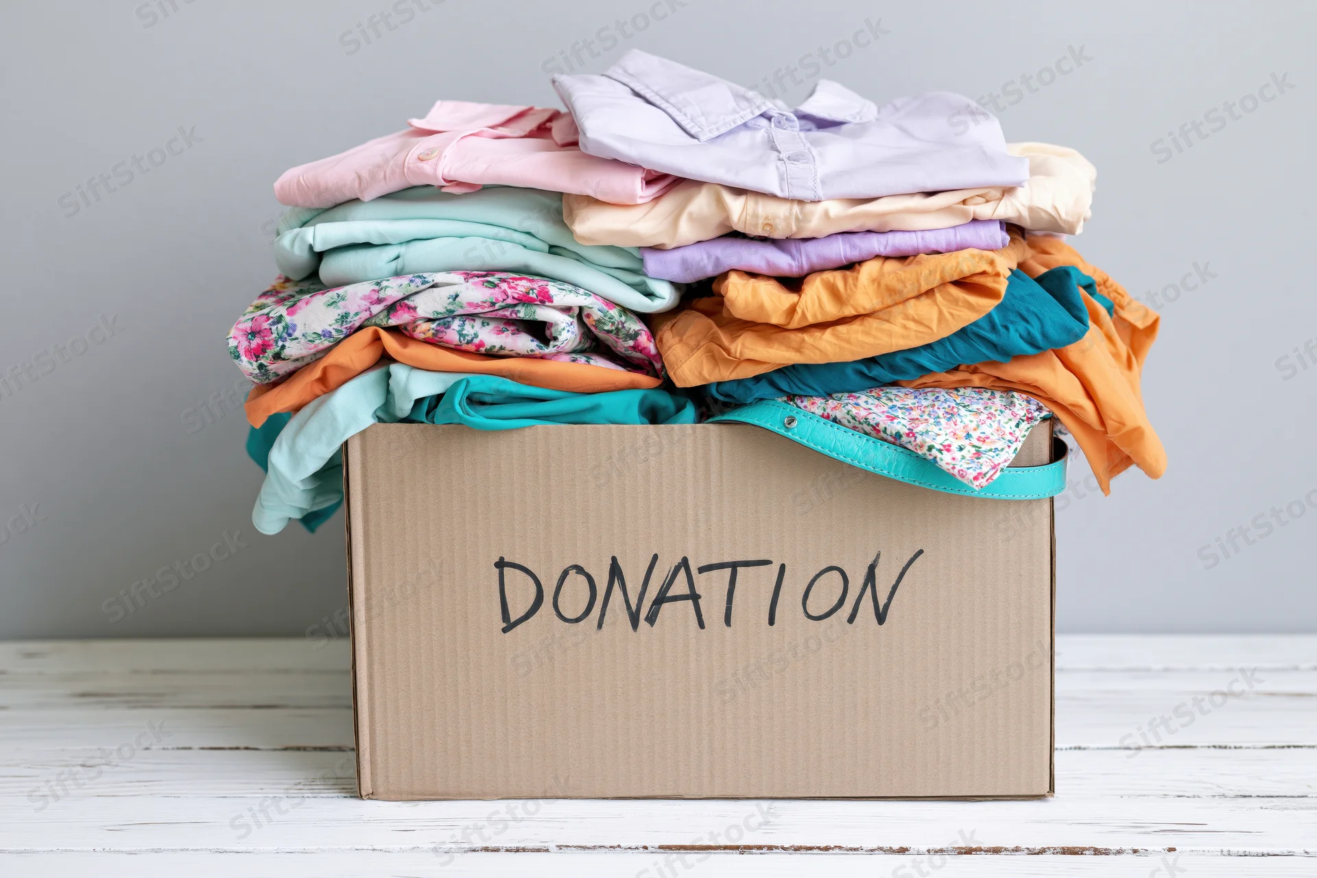 Cardboard box filled with folded clothing labeled donation on white wooden surface