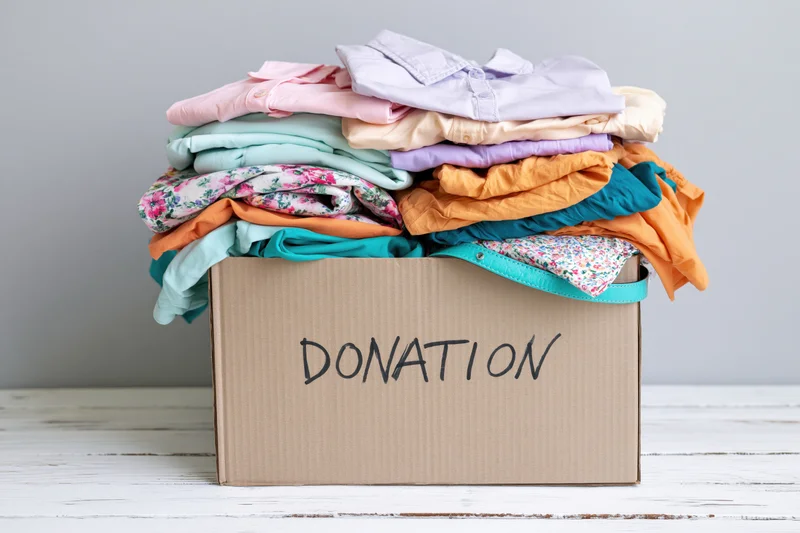 Cardboard box filled with folded clothing labeled donation on white wooden surface