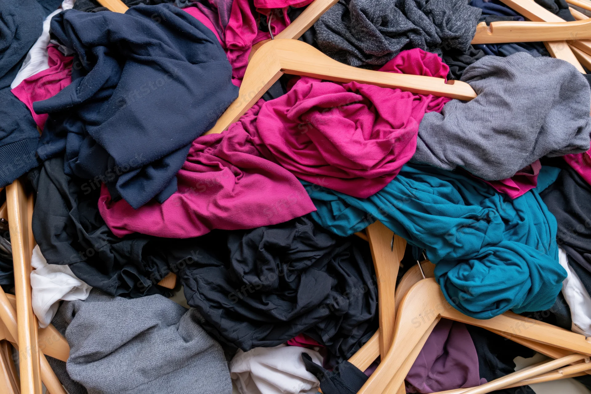 Chaotic pile of mixed clothing and wooden hangers dumped together