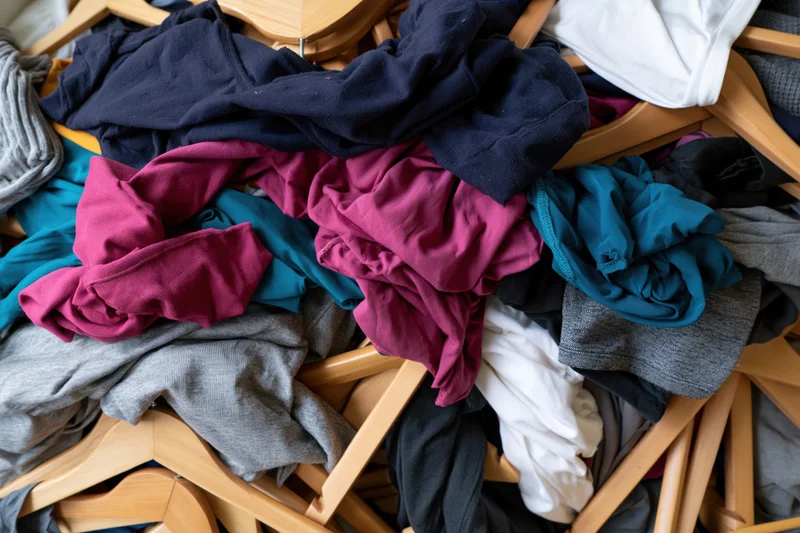 Chaotic pile of mixed clothing and wooden hangers dumped together