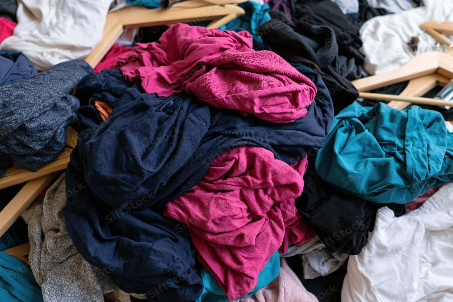 Chaotic pile of mixed clothing and wooden coat hangers dumped together in a heap