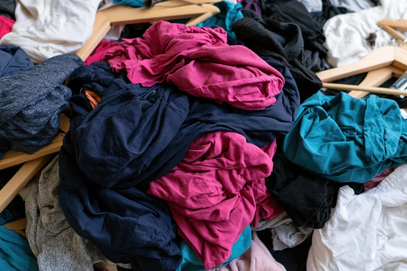 Chaotic pile of mixed clothing and wooden coat hangers dumped together in a heap