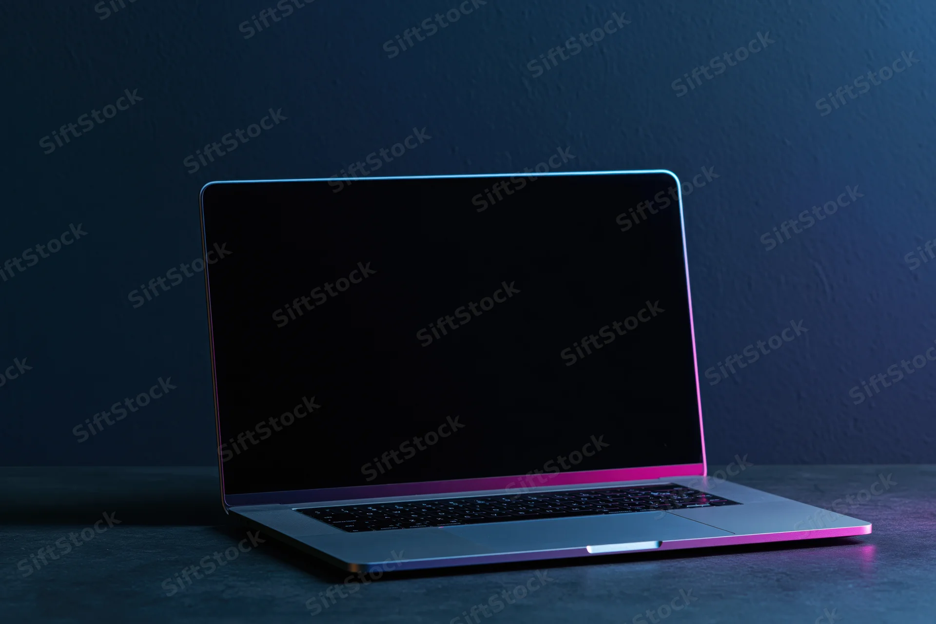 Open laptop with blank screen on dark surface under neon lighting