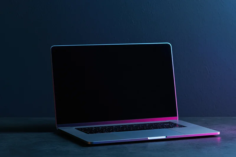 Open laptop with blank screen on dark surface under neon lighting