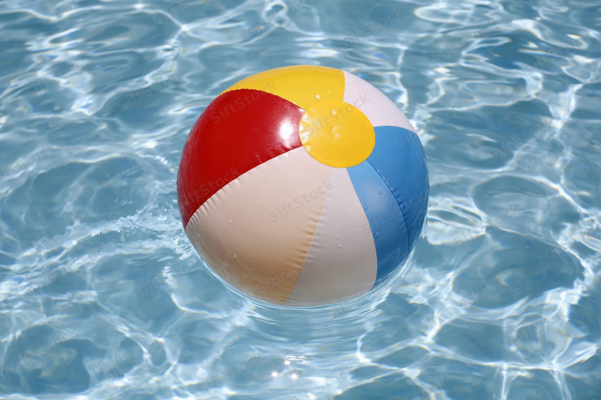 Colorful inflatable beach ball floating in clear blue pool water