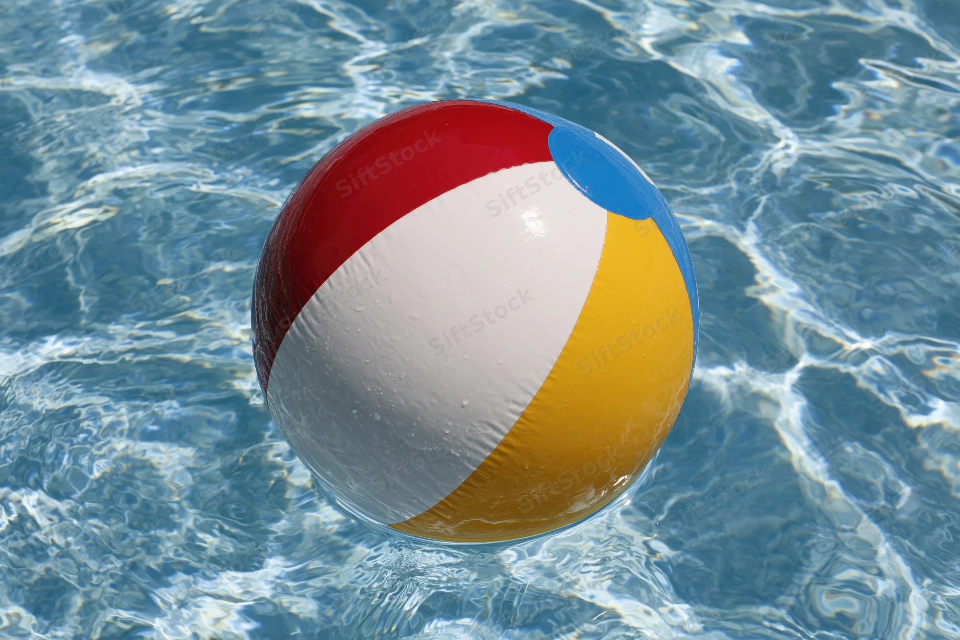 Colorful inflatable beach ball floating in clear blue pool water
