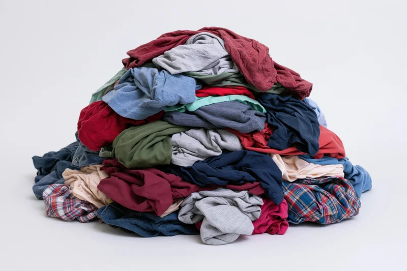 A large messy pile of mixed clothing heaped into a mound on a white surface