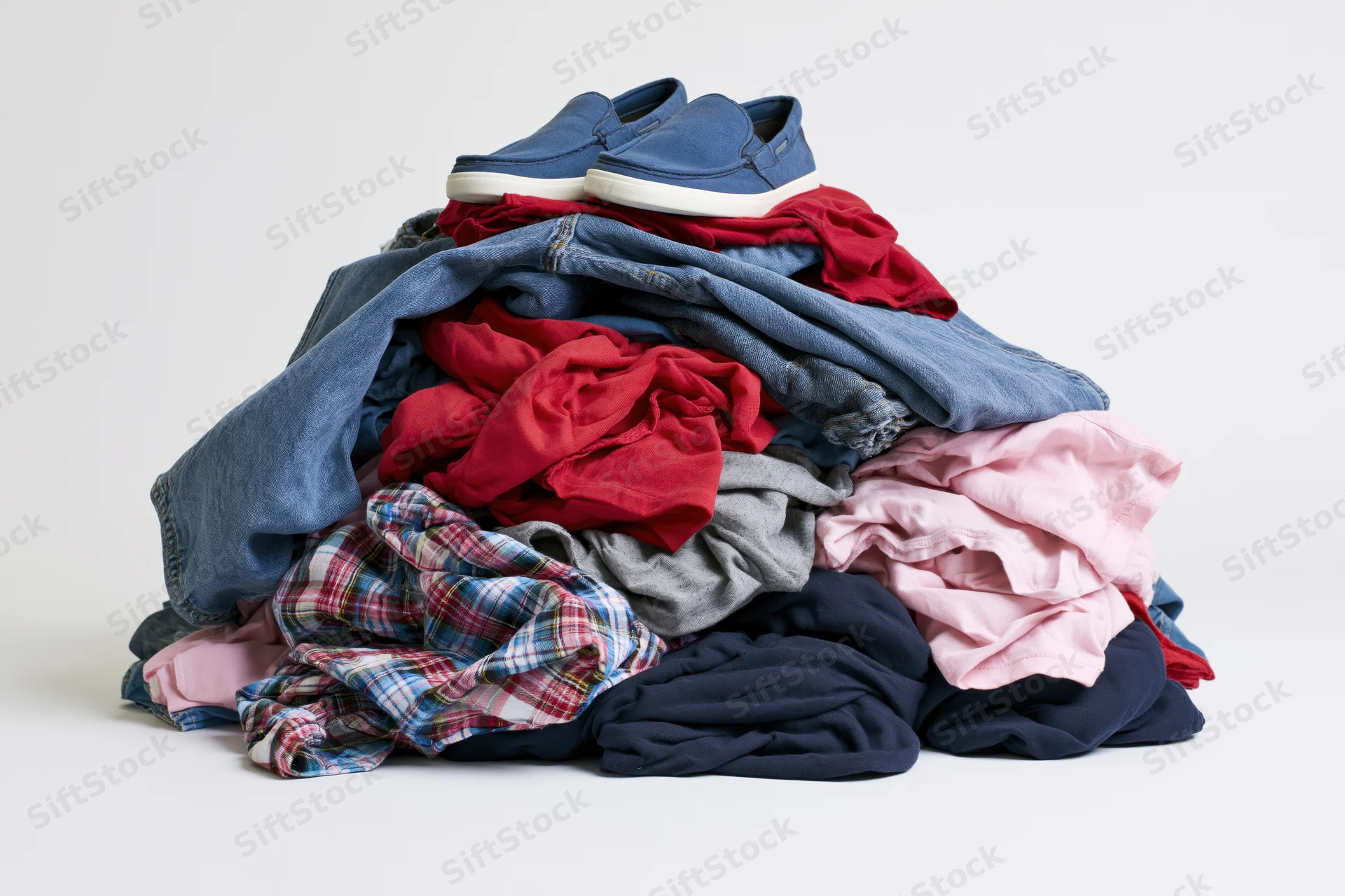 Messy pile of mixed clothing and shoes heaped together on white background