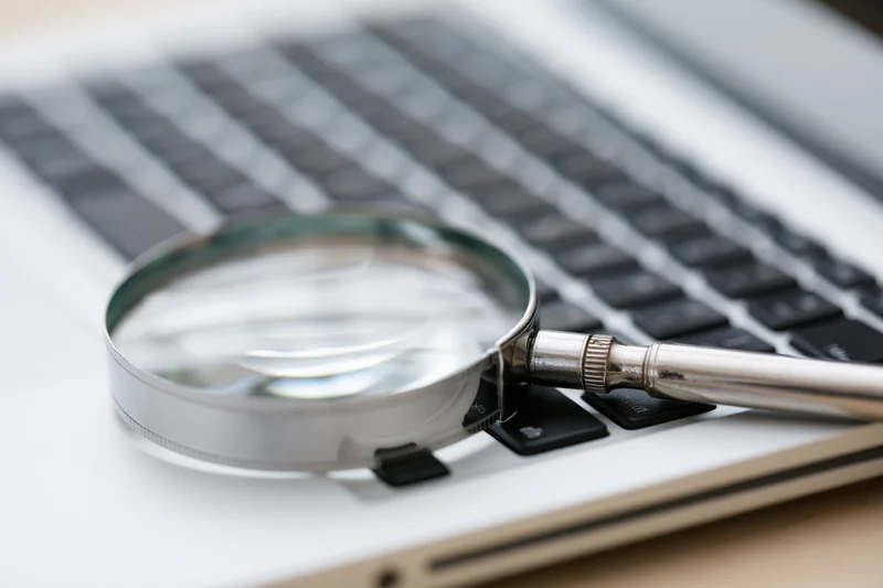 Magnifying glass resting on laptop keyboard in office workspace