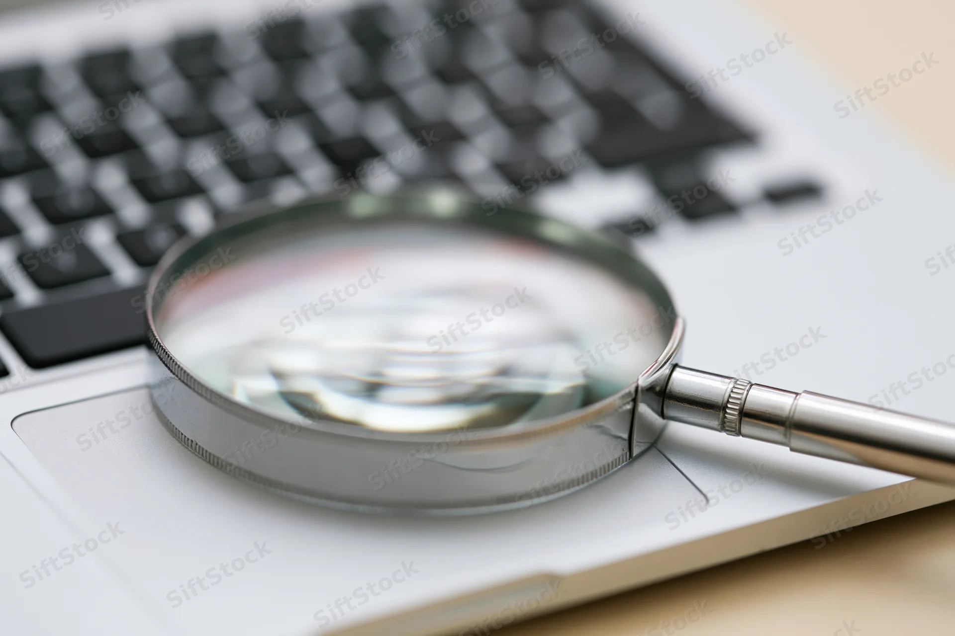 Magnifying glass resting on laptop keyboard in office workspace