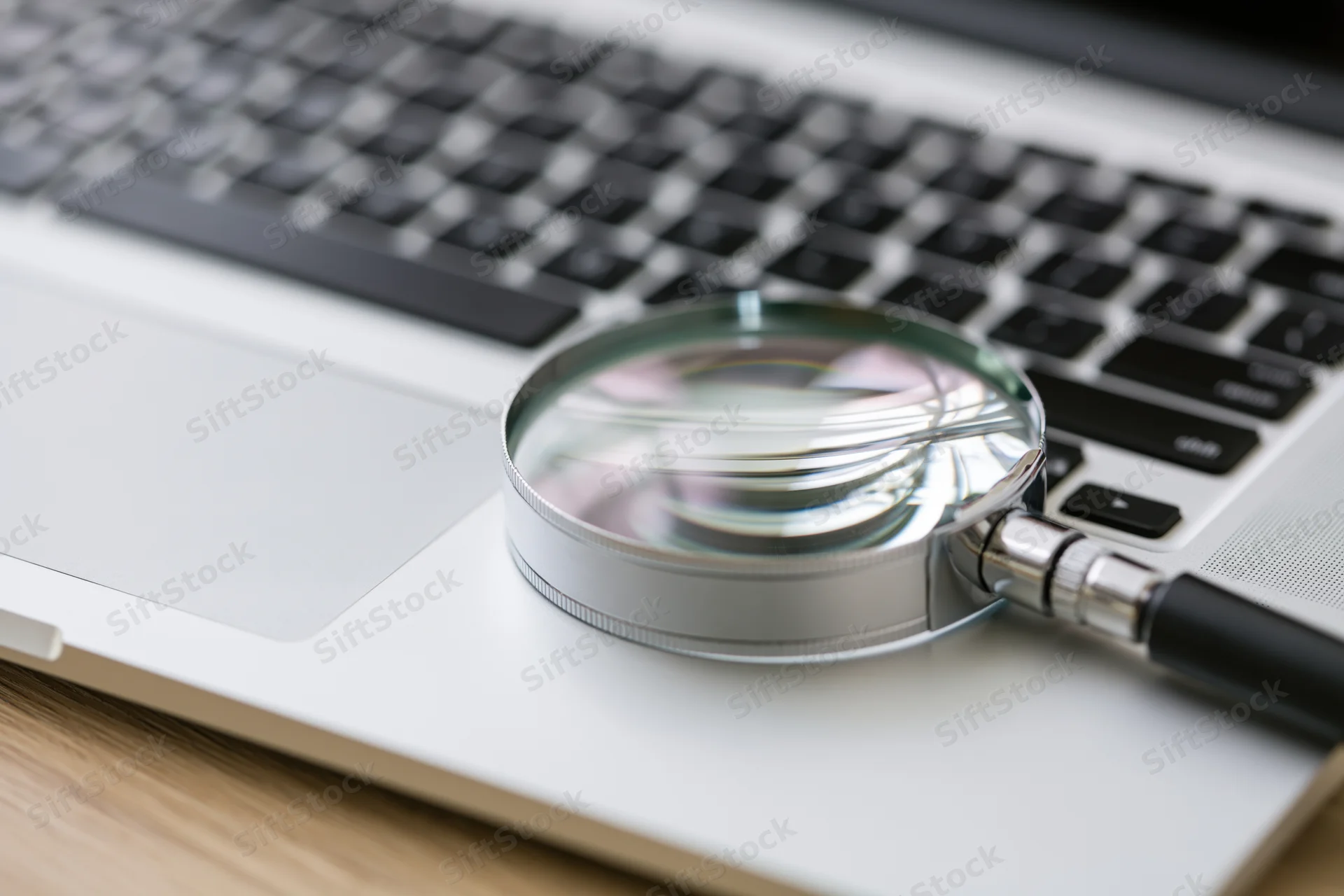 Magnifying glass resting on a silver laptop keyboard in an office workspace