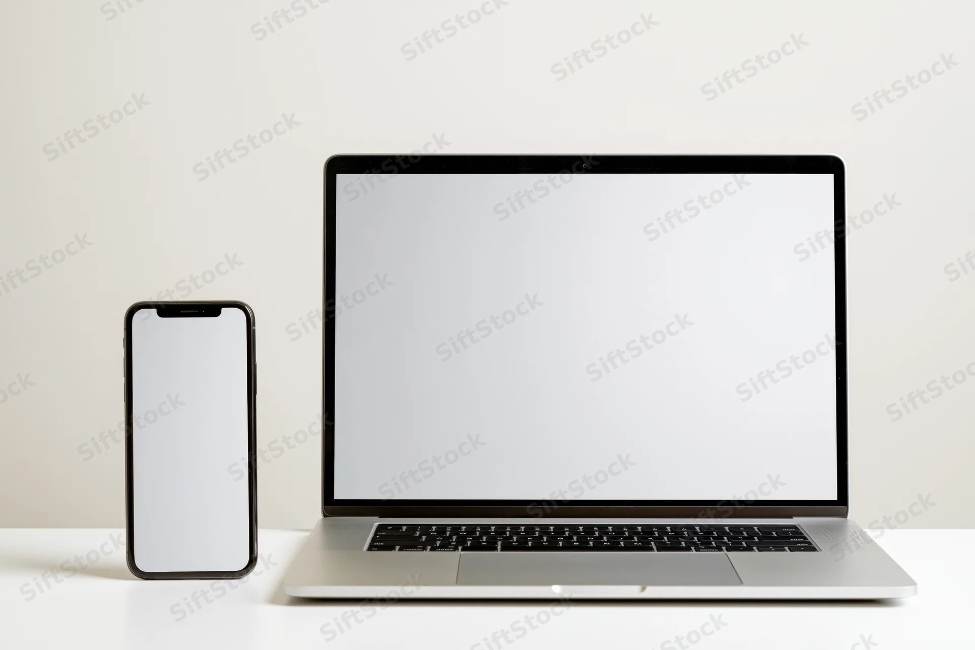 Laptop and smartphone with blank screens on a white surface