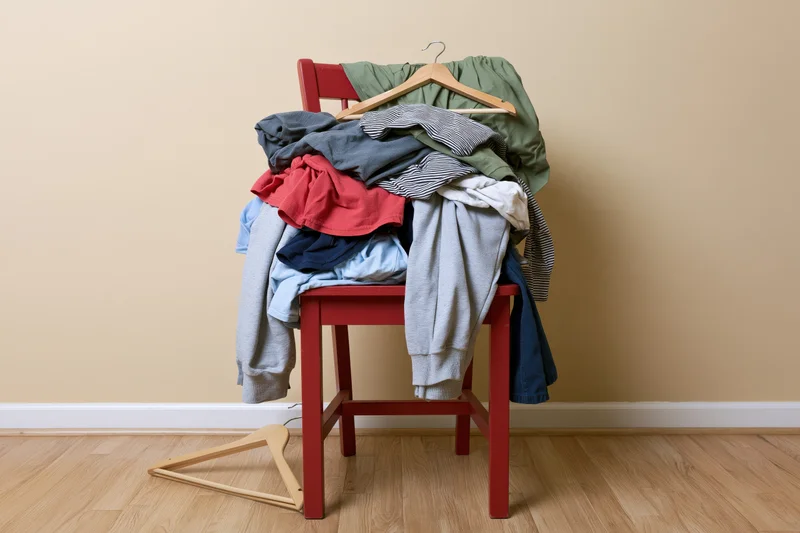 Red wooden chair piled high with casual clothes and hangers in a room