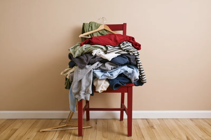 Red wooden chair piled high with casual clothes in a home interior