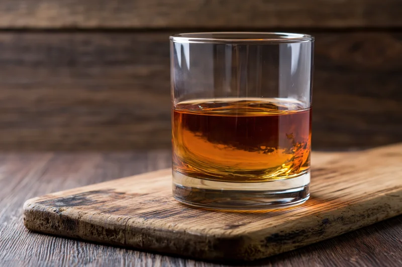 Amber whiskey in a rocks glass on a wooden cutting board