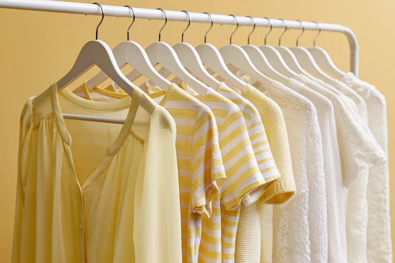 Women's summer clothing hanging on white hangers in a row against a yellow background