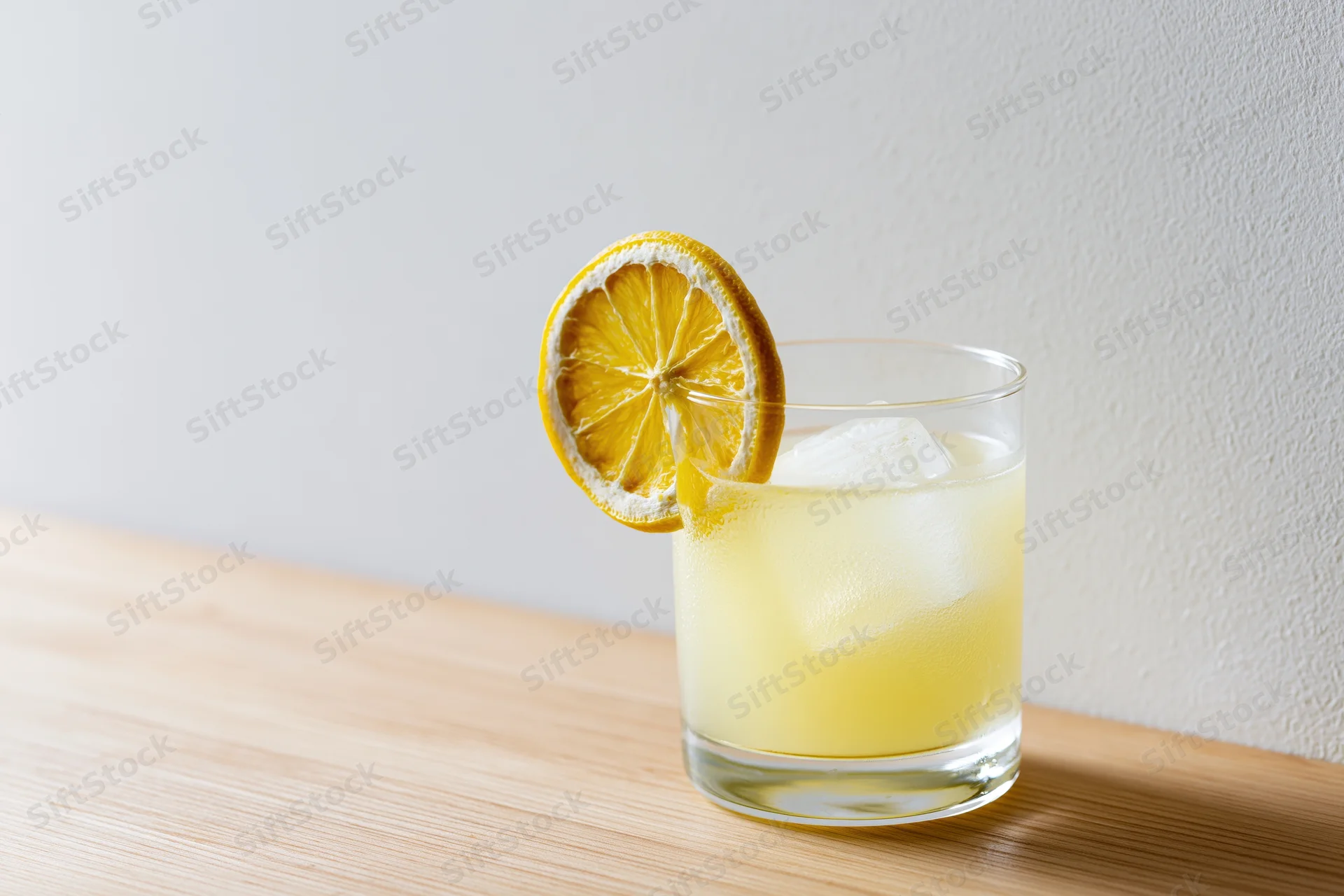 Pale yellow lemonade in a rocks glass with ice and a lemon slice garnish on a wooden table