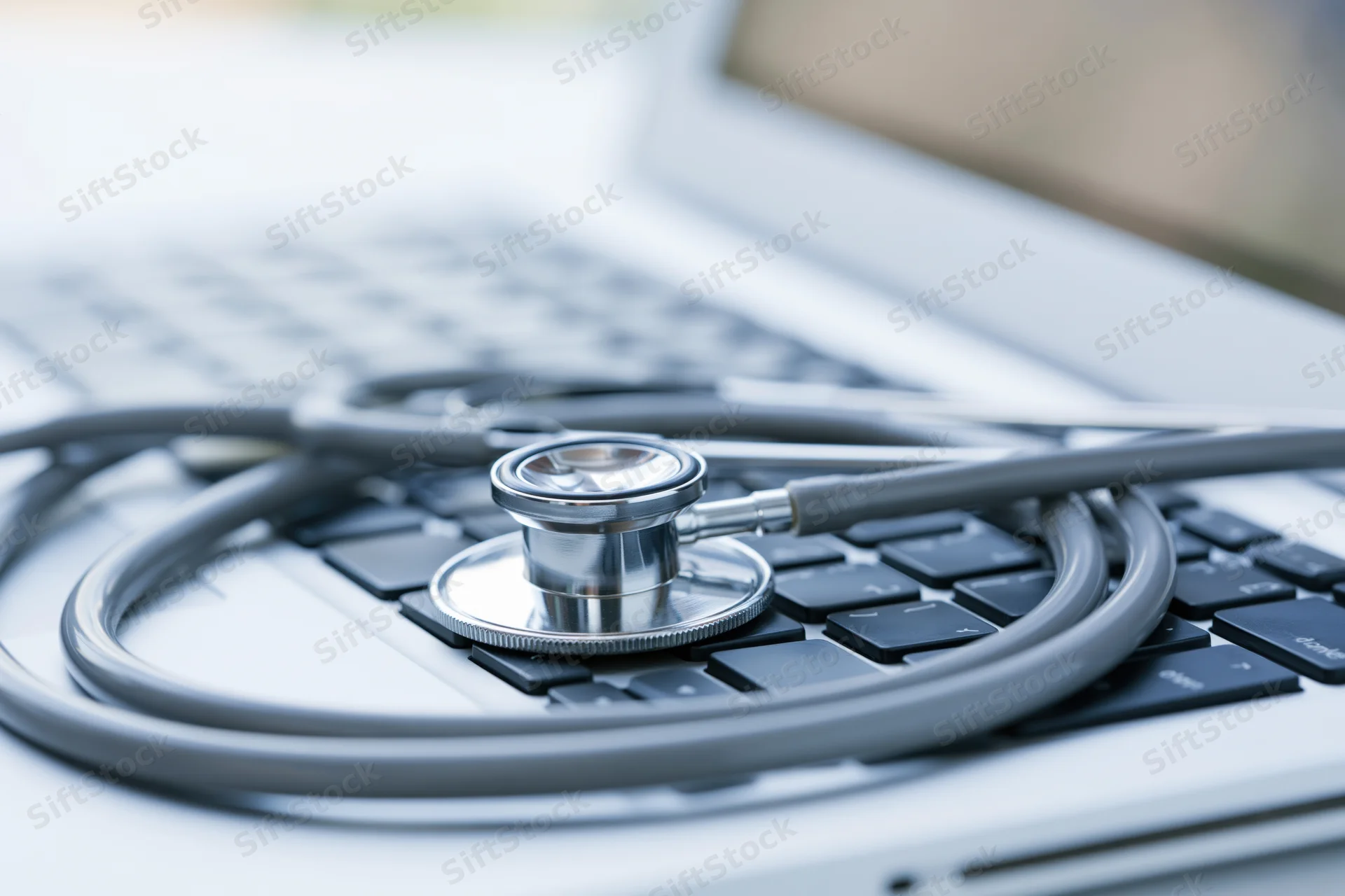 Silver stethoscope resting on laptop keyboard in a medical workspace
