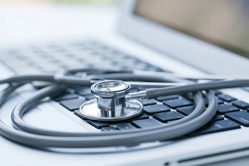 Silver stethoscope resting on laptop keyboard in a medical workspace
