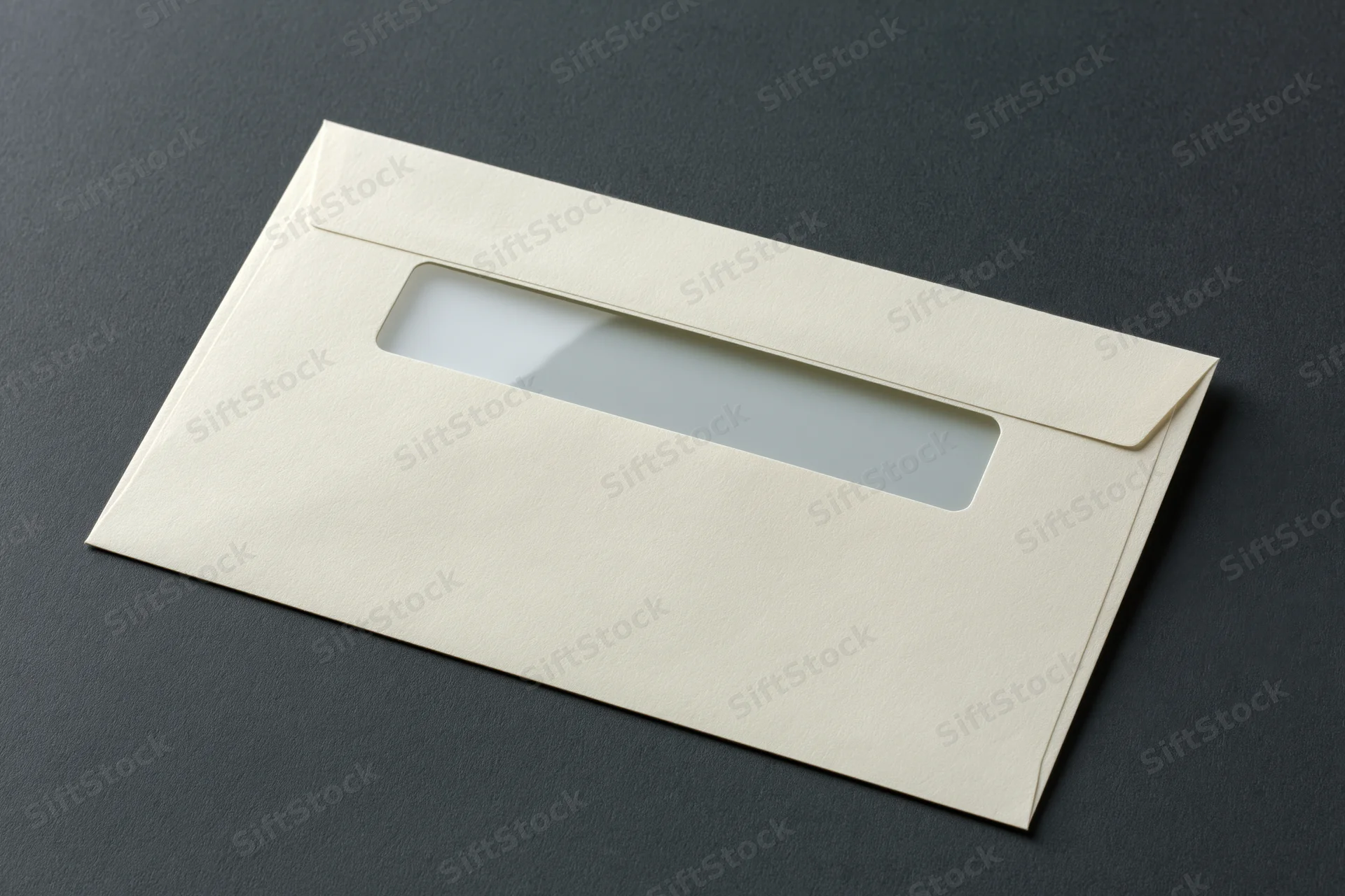 Cream business envelope with window flap lying flat on dark surface