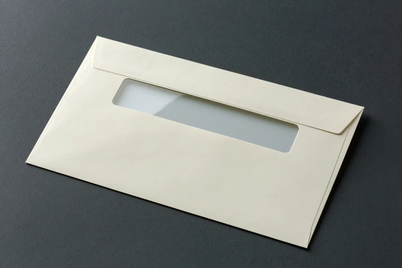 Cream business envelope with window flap lying flat on dark surface