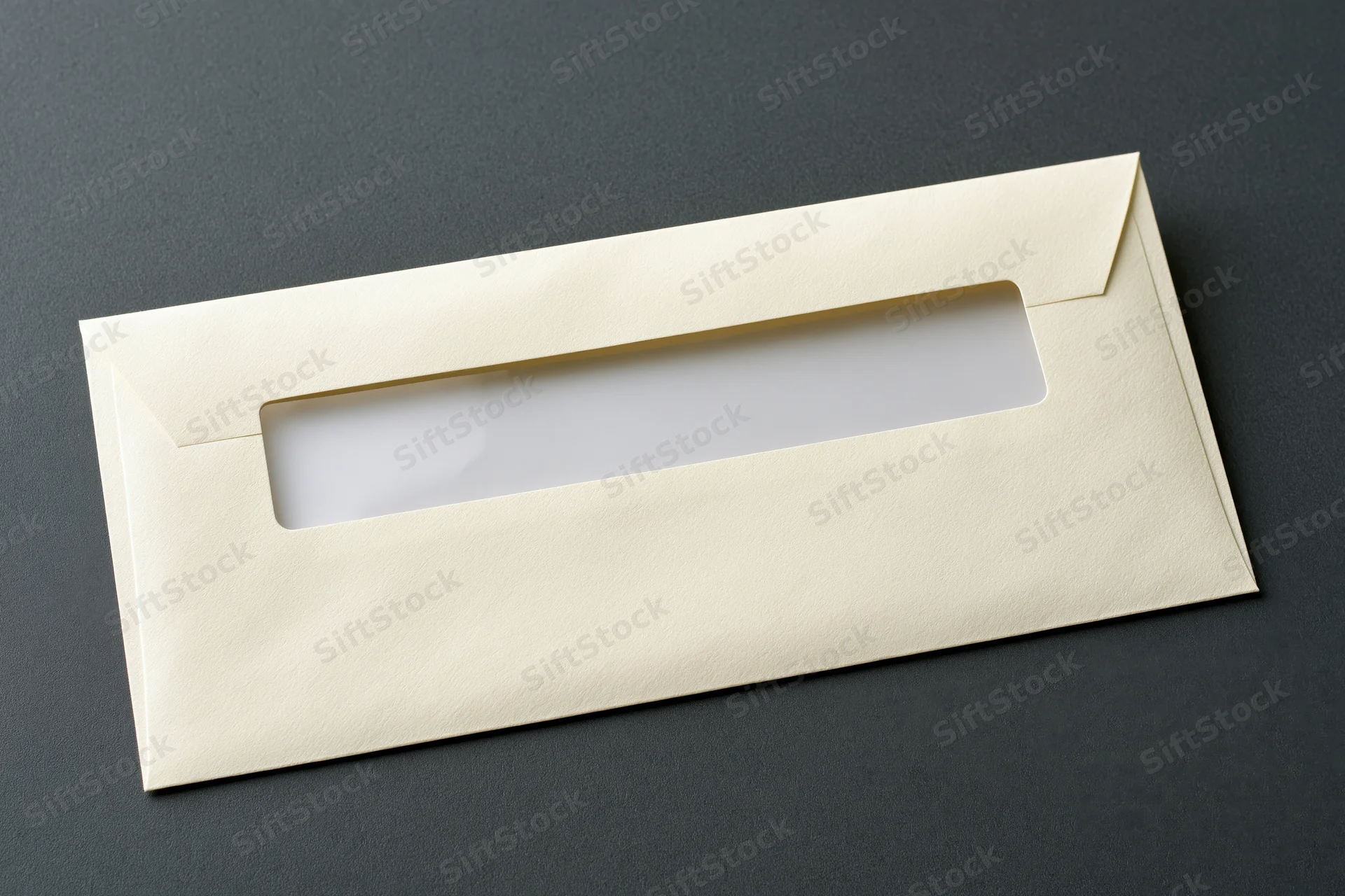 Cream business envelope with window flap closed on dark textured surface