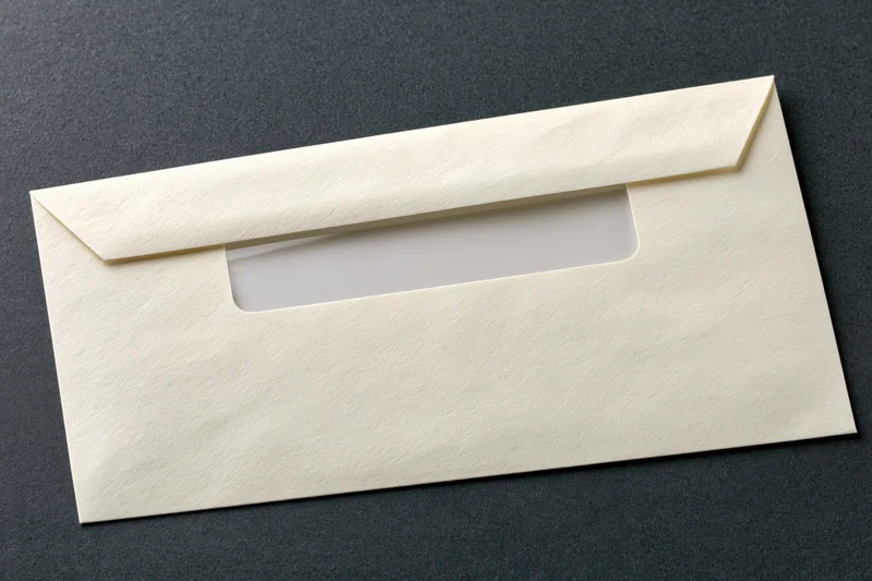 Cream-colored business envelope with window flap lying flat on dark textured surface