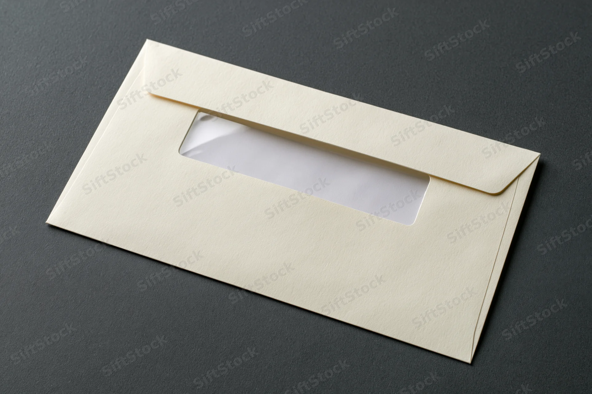 Cream business envelope with window flap lying flat on dark surface