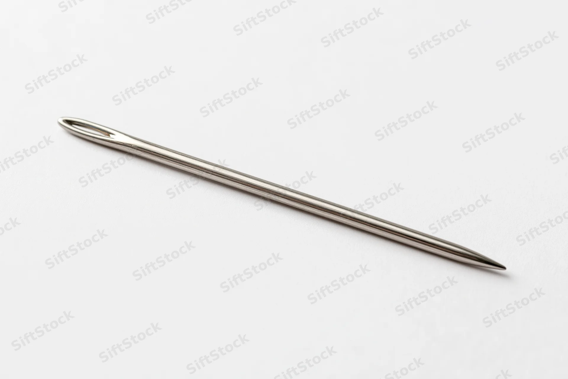 Single steel sewing needle lying diagonally on plain white surface