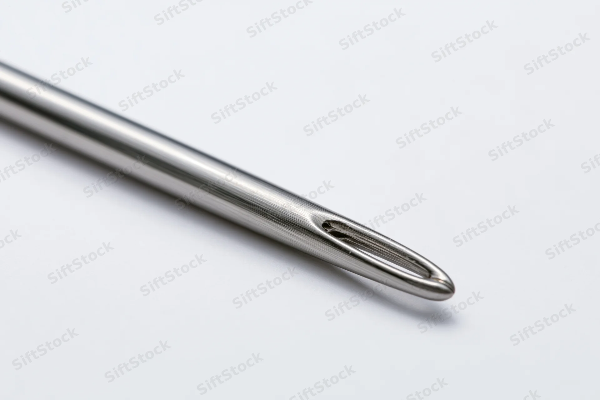 Steel sewing needle lying diagonally on white surface