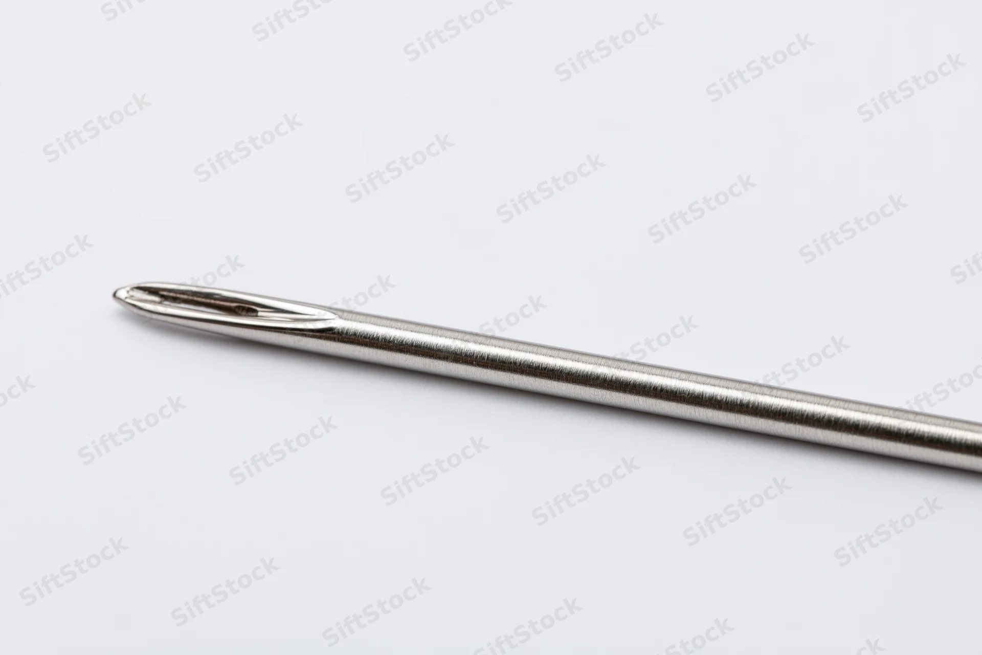 Single steel sewing needle lying diagonally on white background