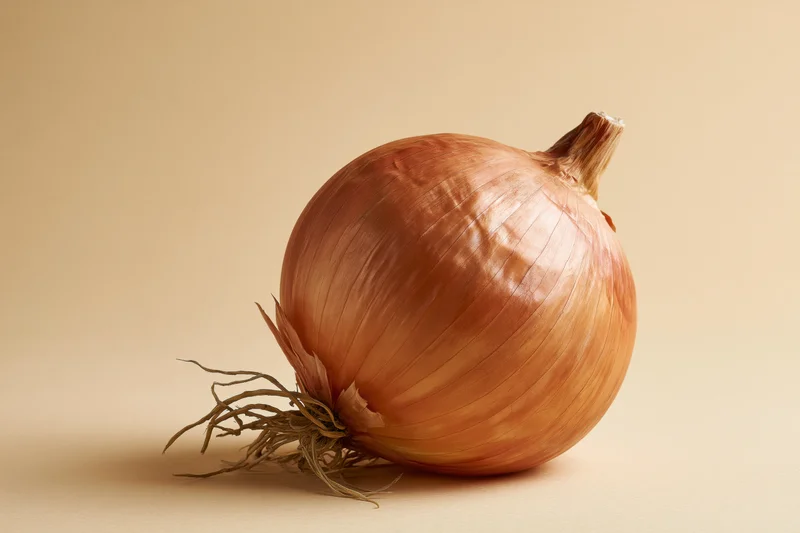 Whole yellow onion resting on a neutral surface in studio lighting