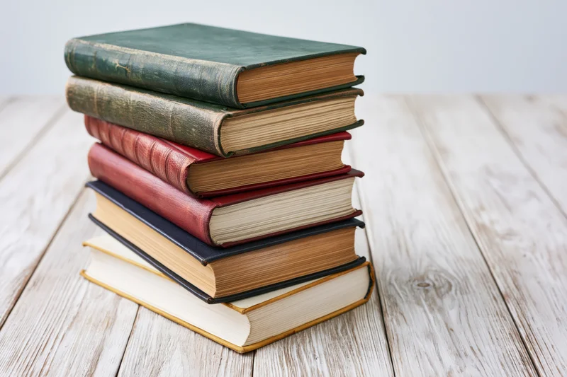 Stack of worn hardcover books on a wooden table
