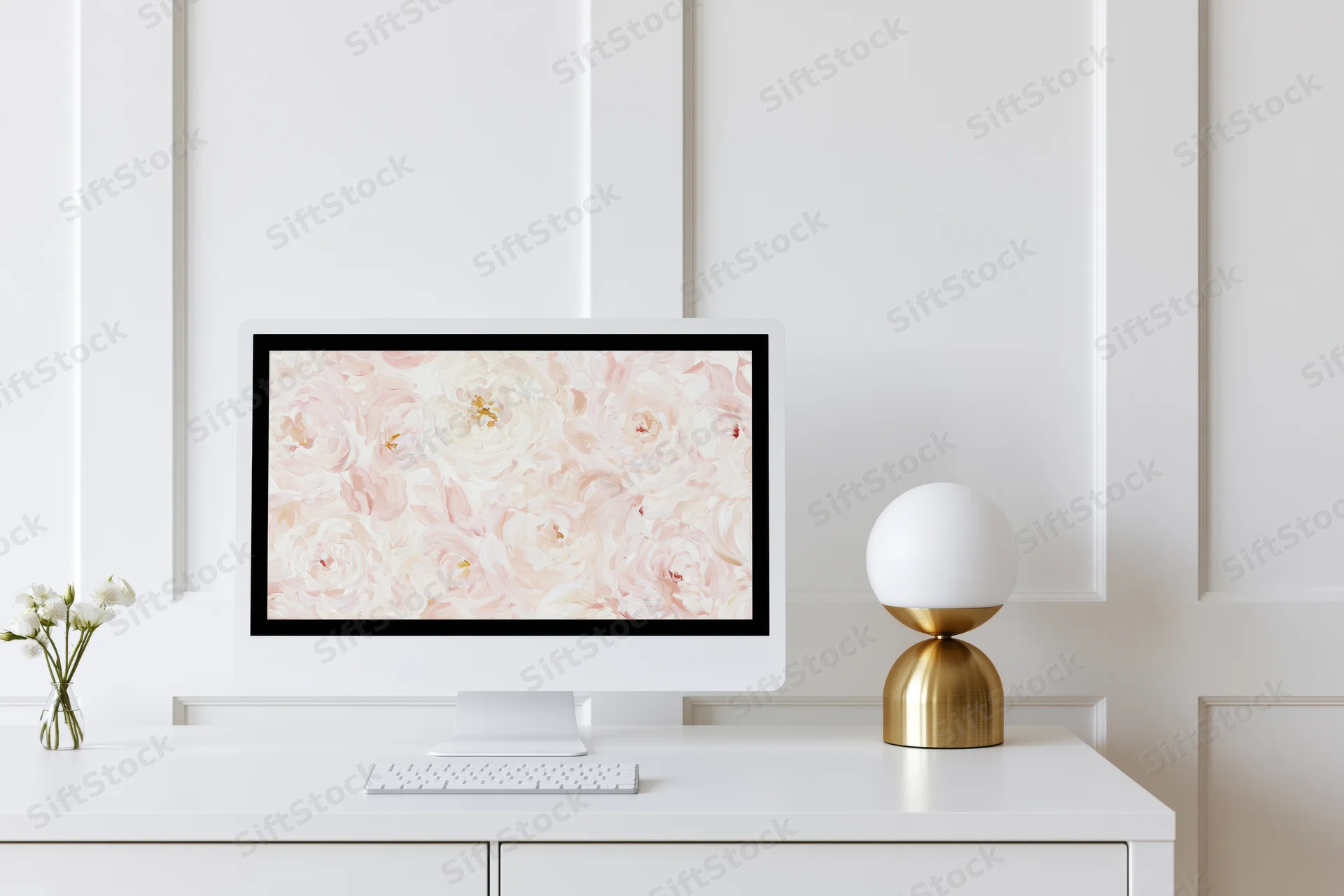 White desktop computer displaying floral wallpaper on a minimalist white desk with a gold lamp and small vase of flowers