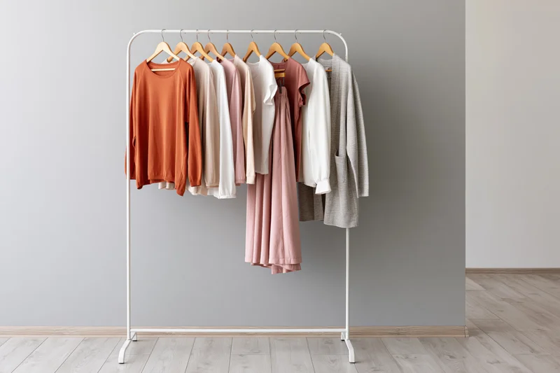 White metal clothing rack holding casual garments in neutral tones against gray wall in minimalist room