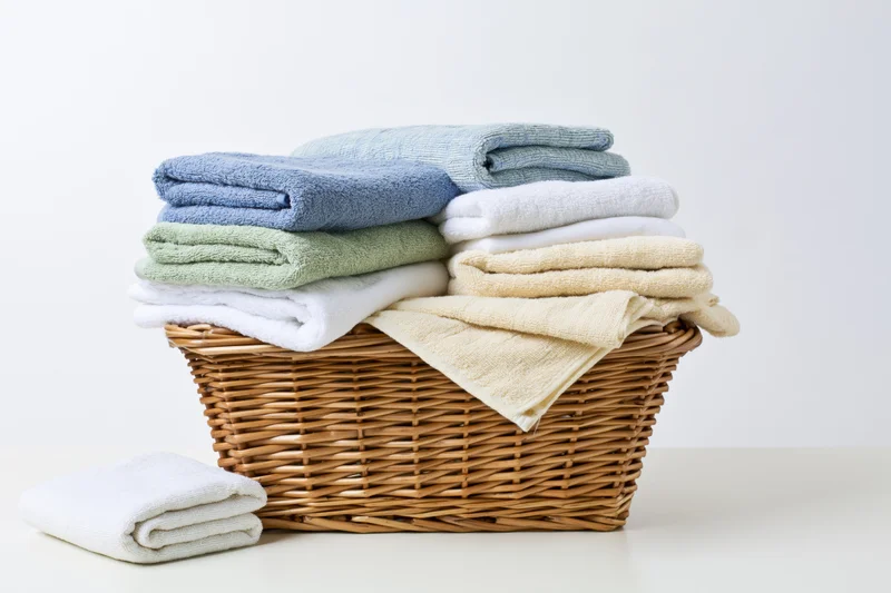 Woven wicker laundry basket filled with neatly folded terry towels in pastel colors on a white surface