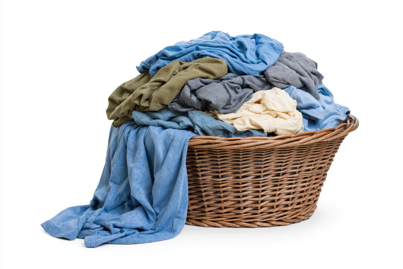 Wicker laundry basket overflowing with crumpled clothes on white background